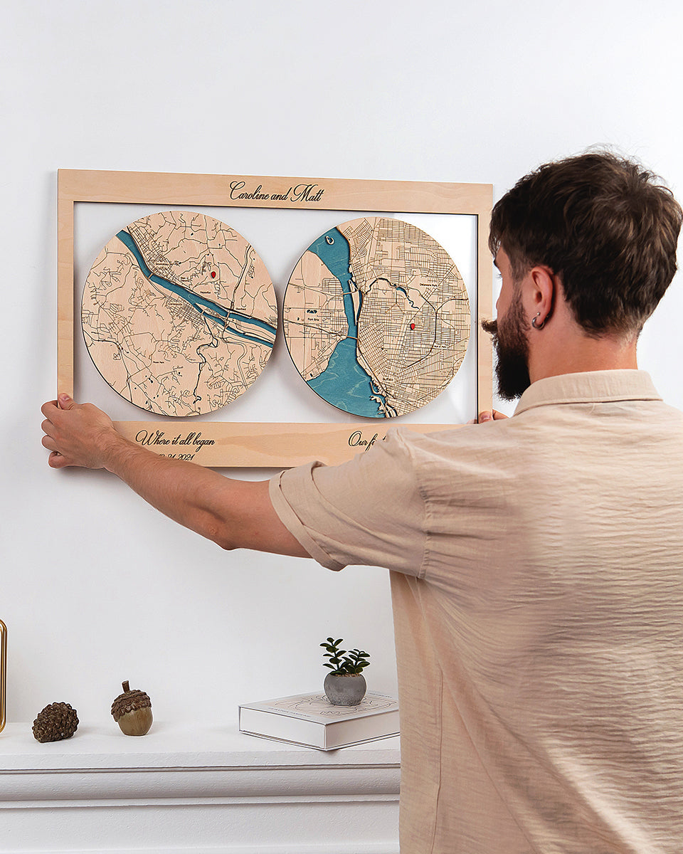 Man holding a wooden framed map of two locations against a white wall.