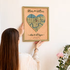 Person hanging a romantic personalized anniversary map on the wall, featuring a heart-shaped New Orleans location map, raised names, custom date, and sage frame.