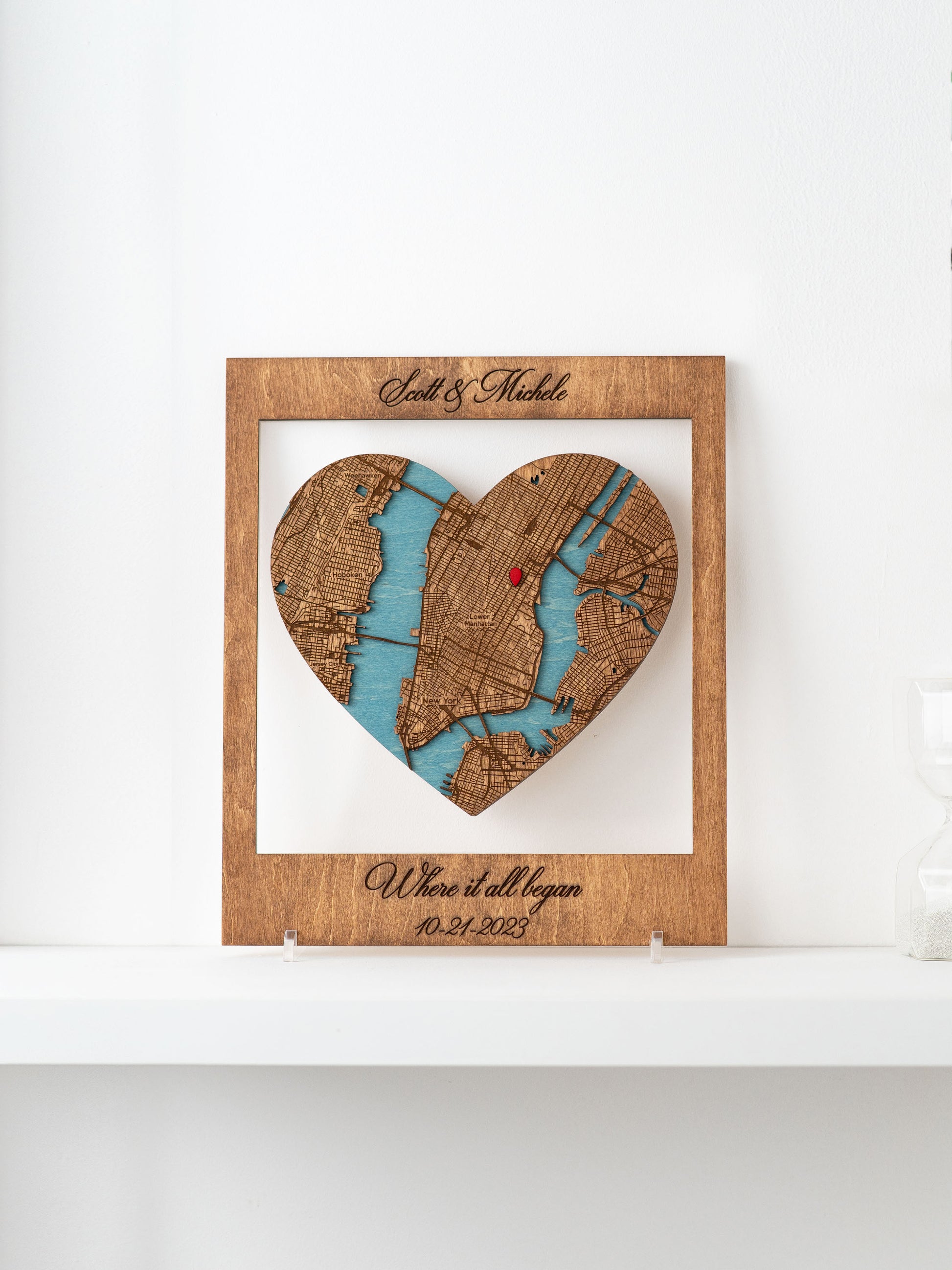A framed Where it all began wooden map cutout in the shape of a heart, with names and a special date marked.