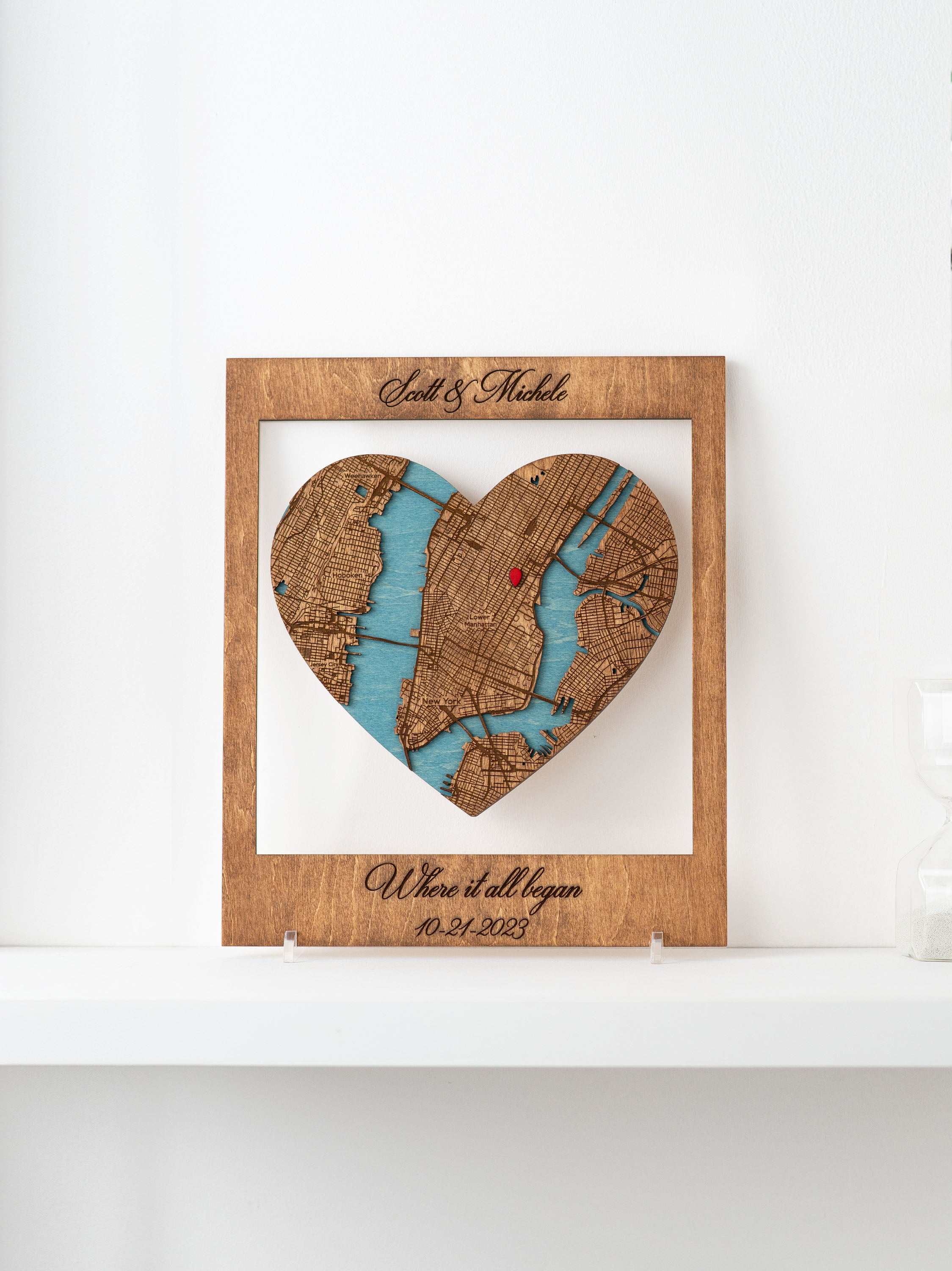 A framed Where it all began wooden map cutout in the shape of a heart, with names and a special date marked.