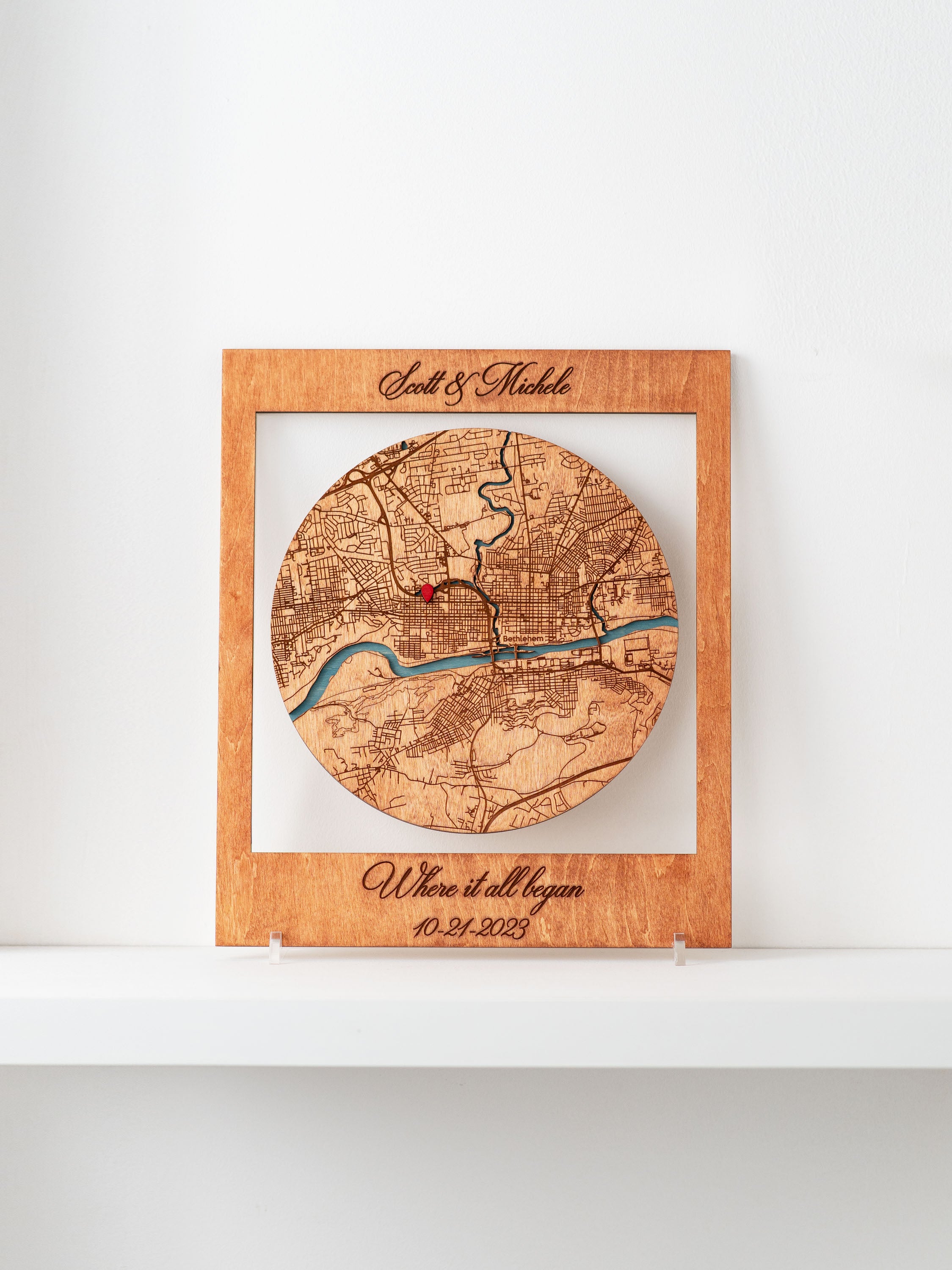 A framed Where it all began wooden map cutout in the shape of a circle, with names and a special date marked.