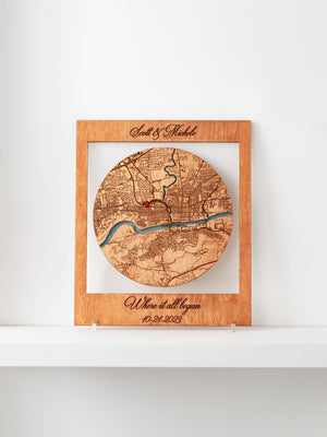 A framed Where it all began wooden map cutout in the shape of a circle, with names and a special date marked.