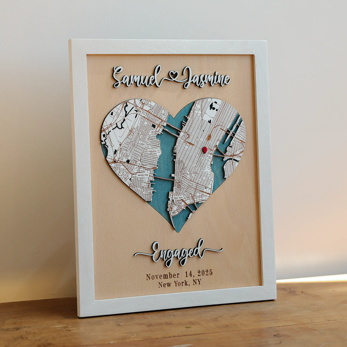 Personalized engagement map gift in white frame with custom New York location, heart-shaped 3D wooden map, raised names, date, and red location marker.
