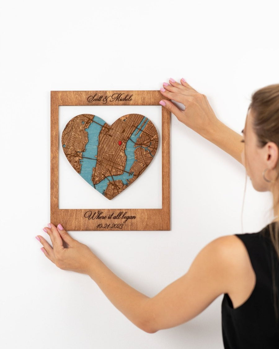 Person holding a wooden heart-shaped frame with a map design on a white background