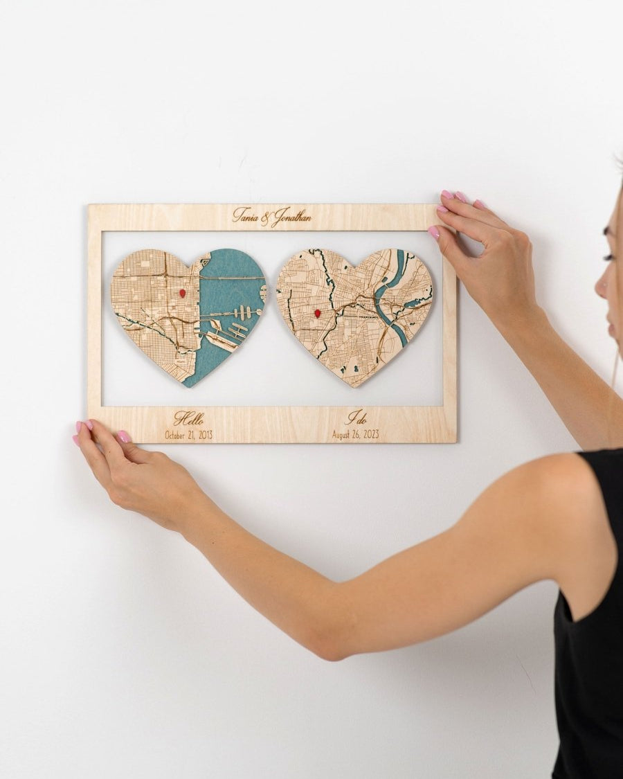 Person holding a wooden frame with heart-shaped cutouts of two maps on a white background