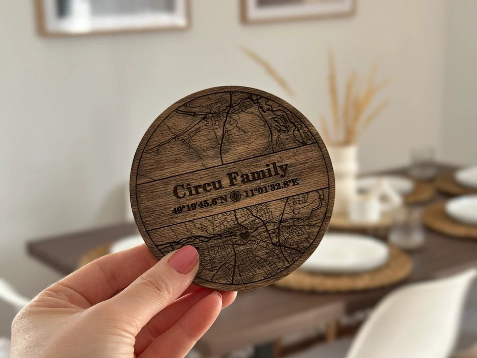 Wooden coaster with engraved design and text held in a hand, with a blurred indoor setting in the background.