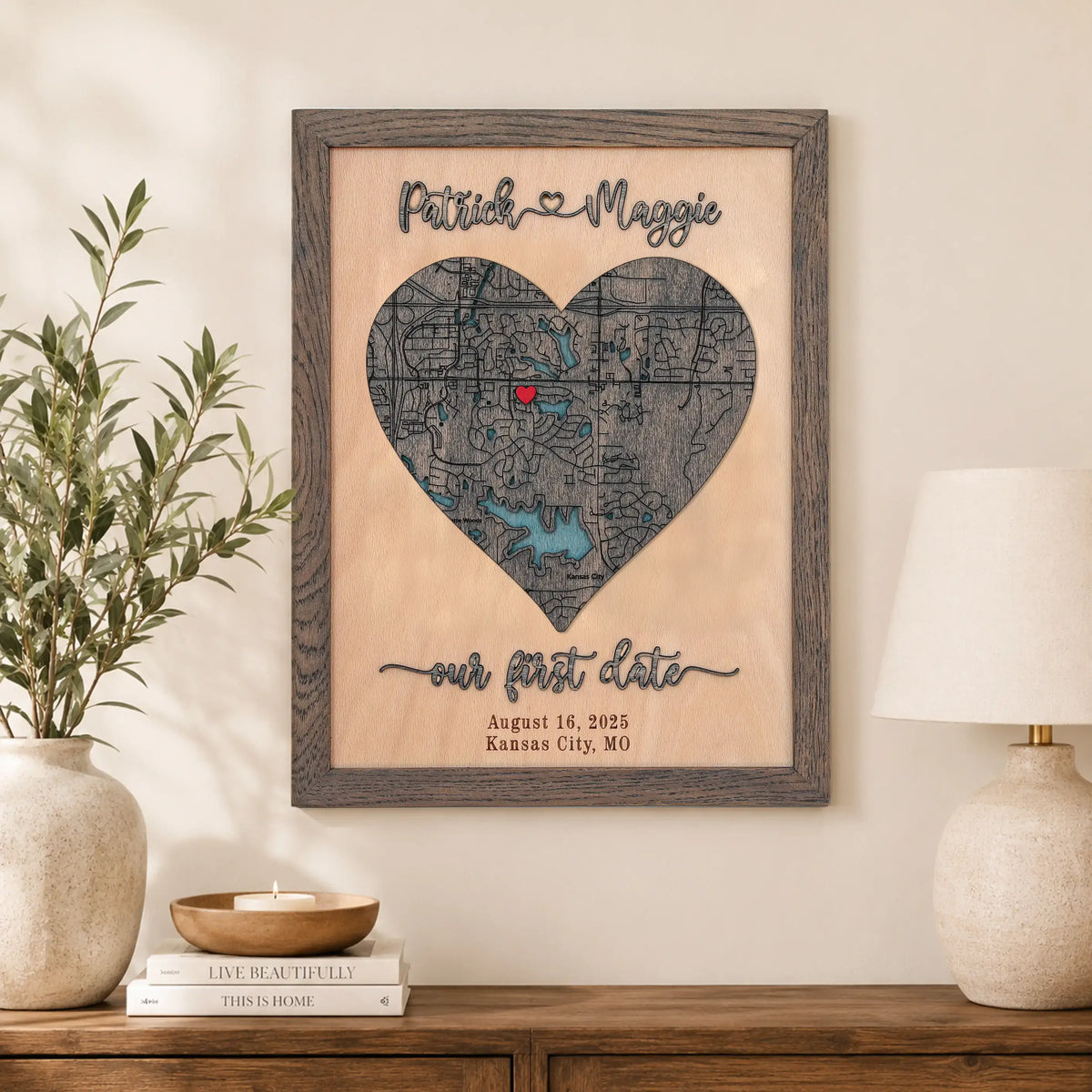 Personalized 3D wooden heart map with custom Kansas City location, raised names, first date details, and grey oak frame in a warm home interior.