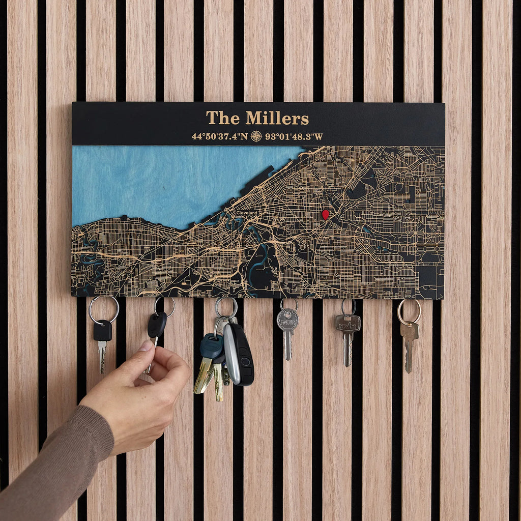 Hand using wooden magnetic key holder for wall with custom coordinates in black finish