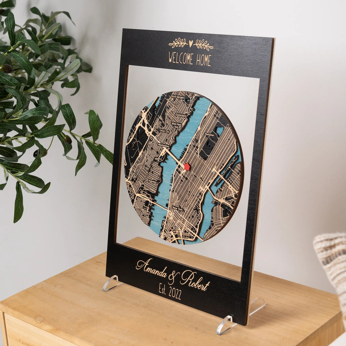 Angled view of custom housewarming gift with layered wooden city map in black frame, personalized new home keepsake for display