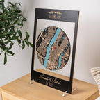Angled view of custom housewarming gift with layered wooden city map in black frame, personalized new home keepsake for display