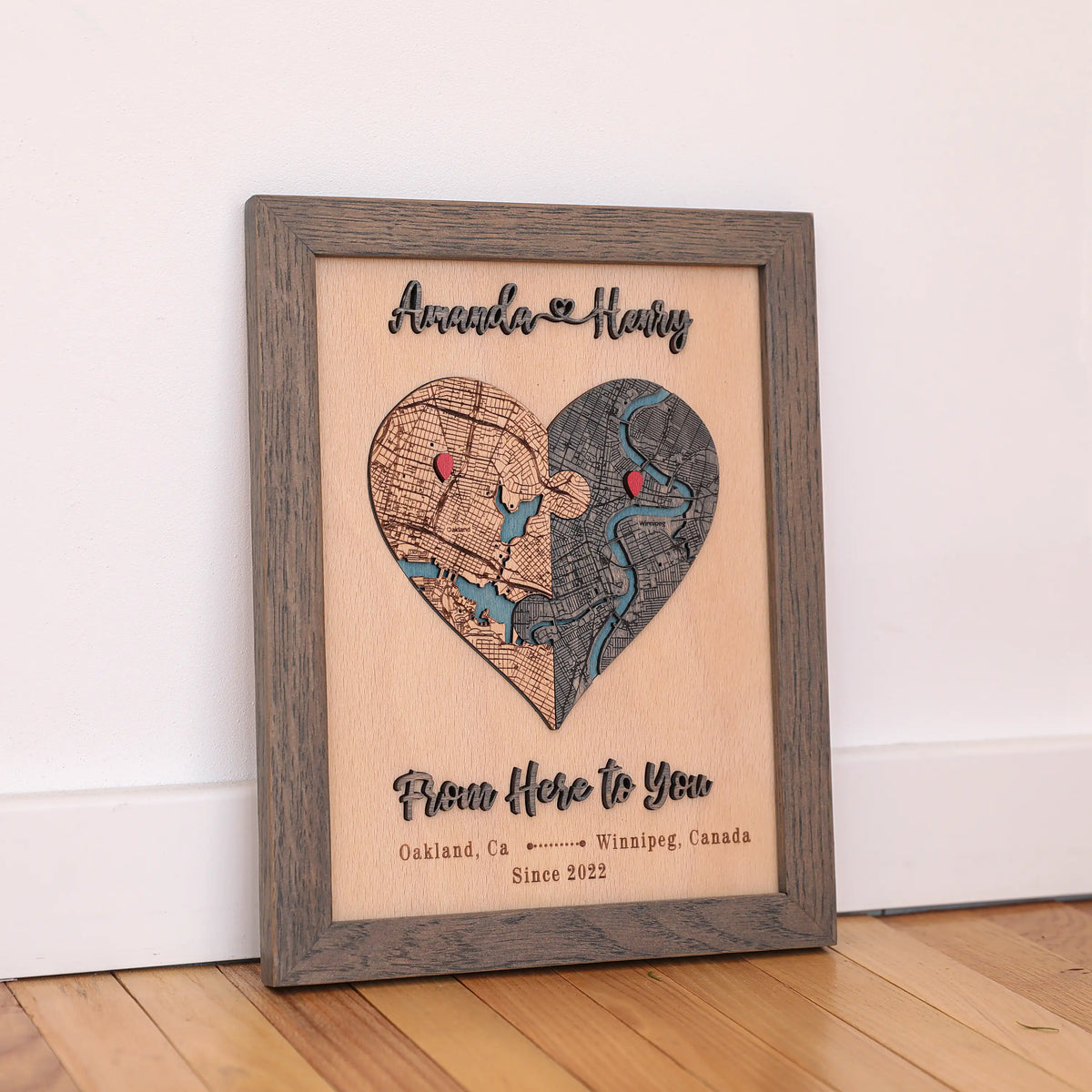 Custom wooden heart map in grey oak frame displayed on a shelf, personalized with two locations and raised names.