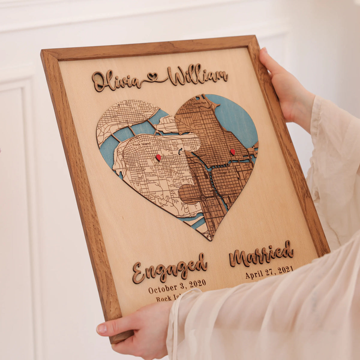 Custom wooden wedding map held in hands, showing heart-shaped personalized locations, raised names, and milestone dates.