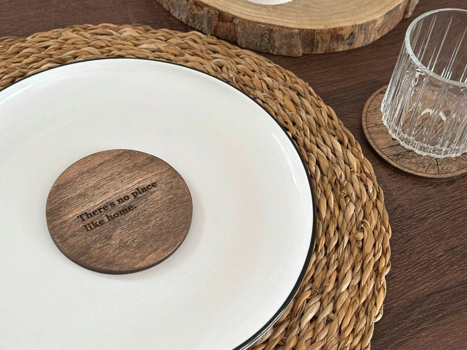 Wooden coaster with 'There's no place like home' text on a white plate with woven placemat.