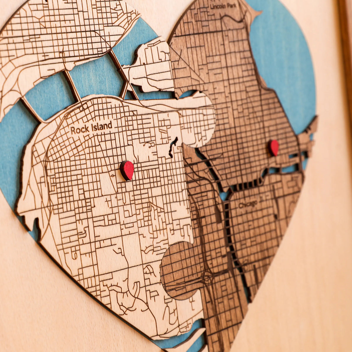 Close-up of heart-shaped wedding map with layered wooden streets, blue water details, red pins, and two custom locations.