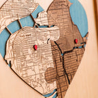 Close-up of heart-shaped wedding map with layered wooden streets, blue water details, red pins, and two custom locations.