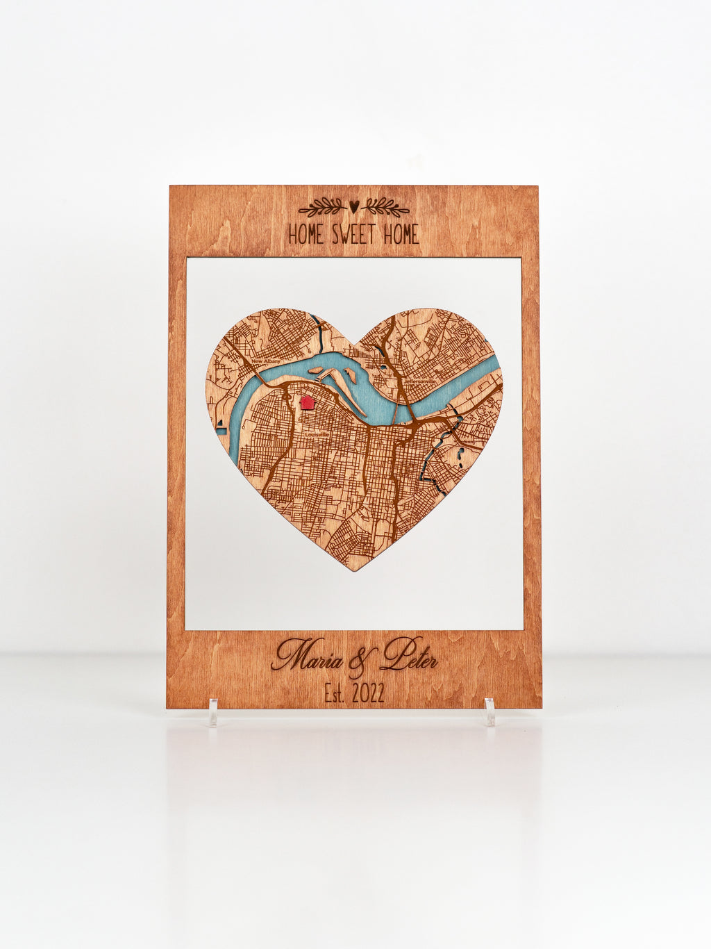 A wooden plaque with a heart-shaped cutout featuring a map design, inscribed with "Home Sweet Home" at the top and "Maria & Peter Est. 2022"  and You can add any text.
