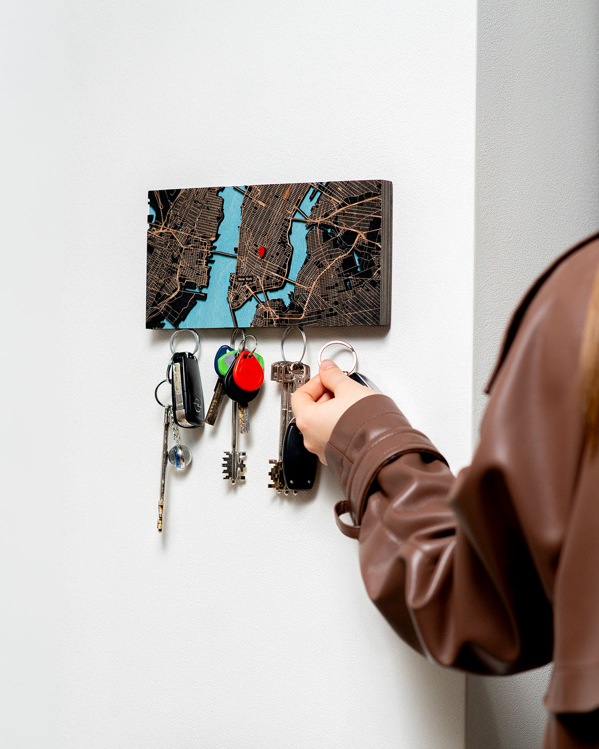 Person hanging keys on a key holder with a map design on a white wall.