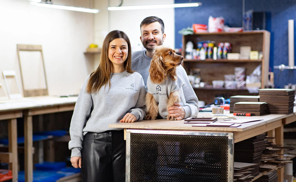 Two members of the MurWoodHome team with a dog at the workshop bench