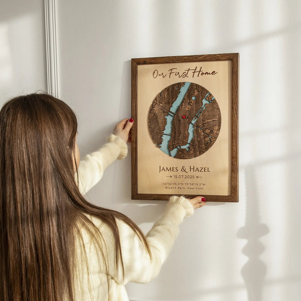 Woman hanging Our First Home Map custom address wall art in solid oak frame with personalized names and first home date