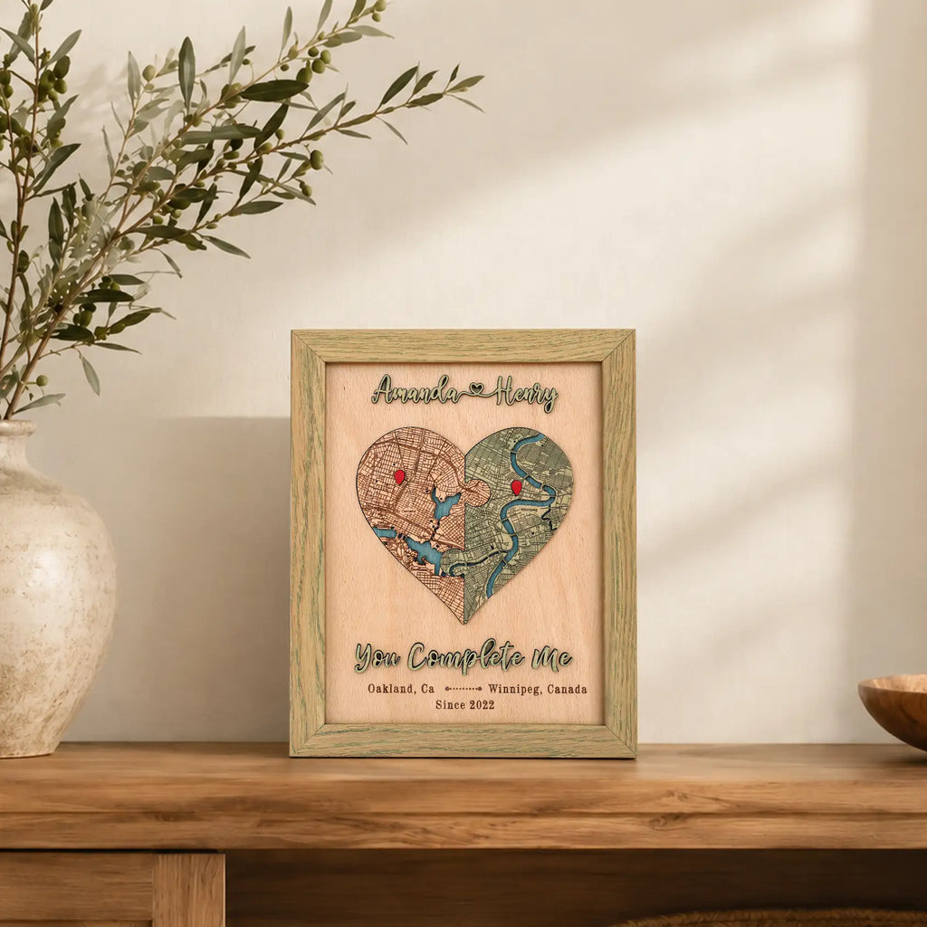 Personalized heart map in sage frame displayed on a wooden shelf, made with two custom locations and raised lettering.