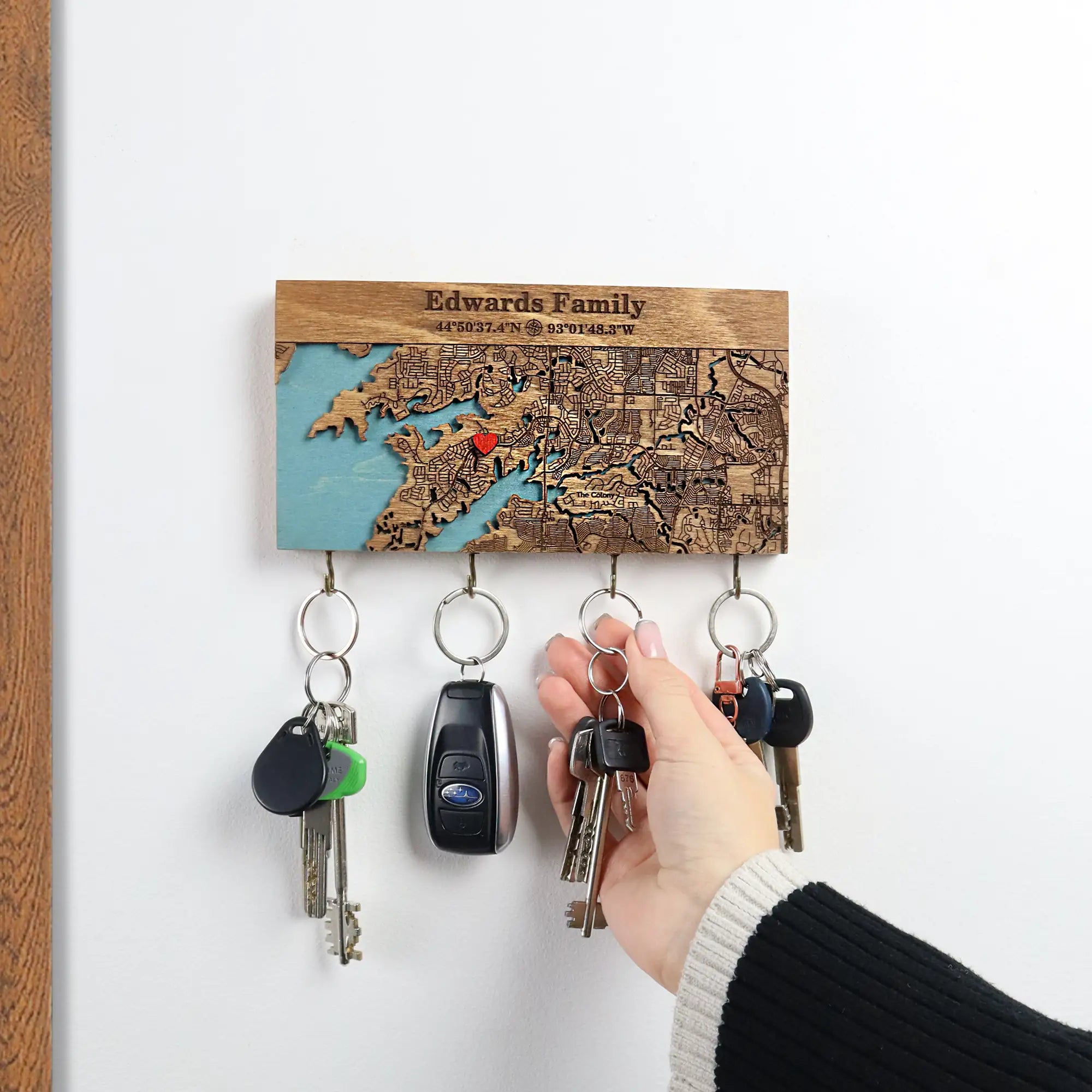 Small personalized wooden key holder with hooks mounted on wall with hand holding keys