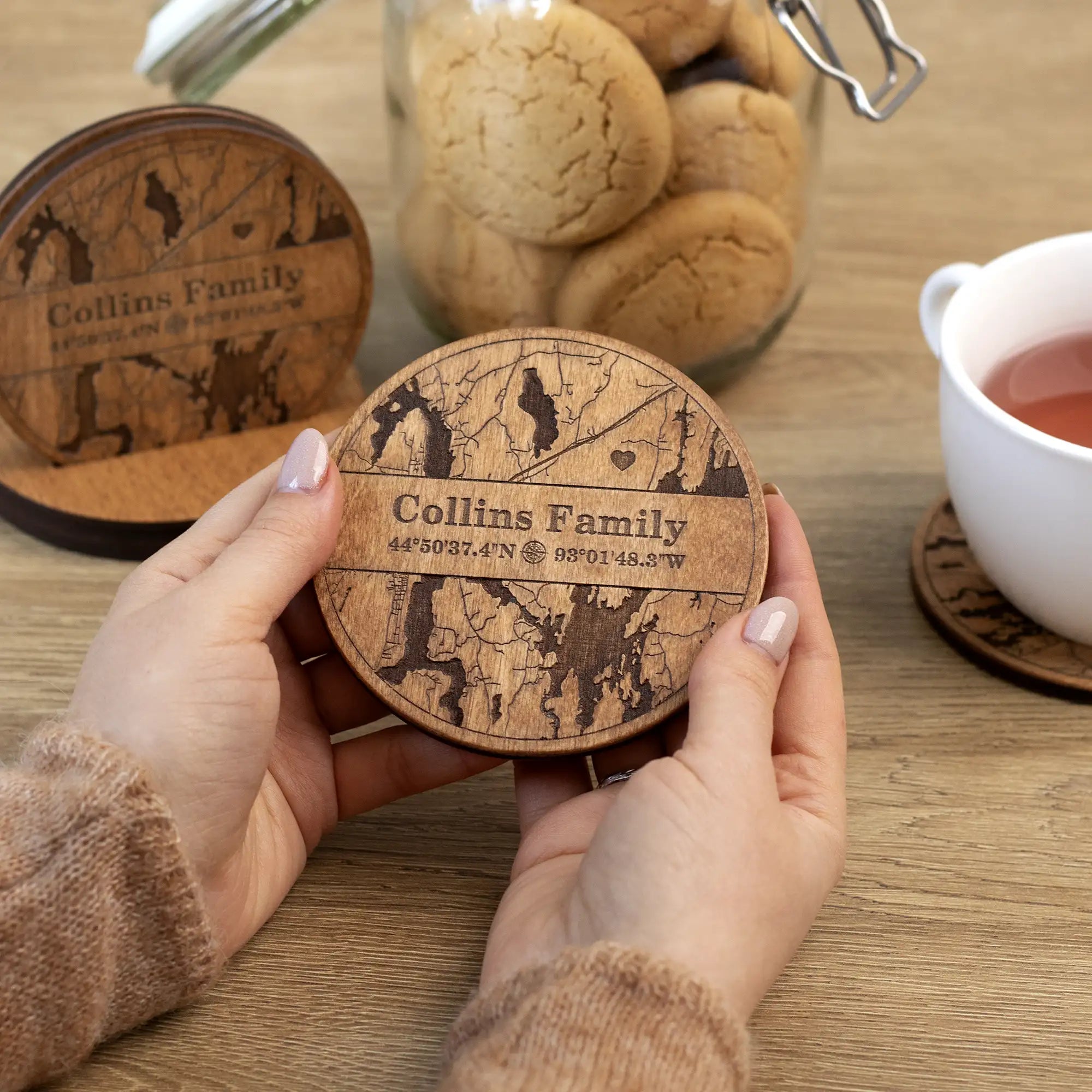 Personalized wooden coaster for housewarming held in hands with engraved family name and home coordinates