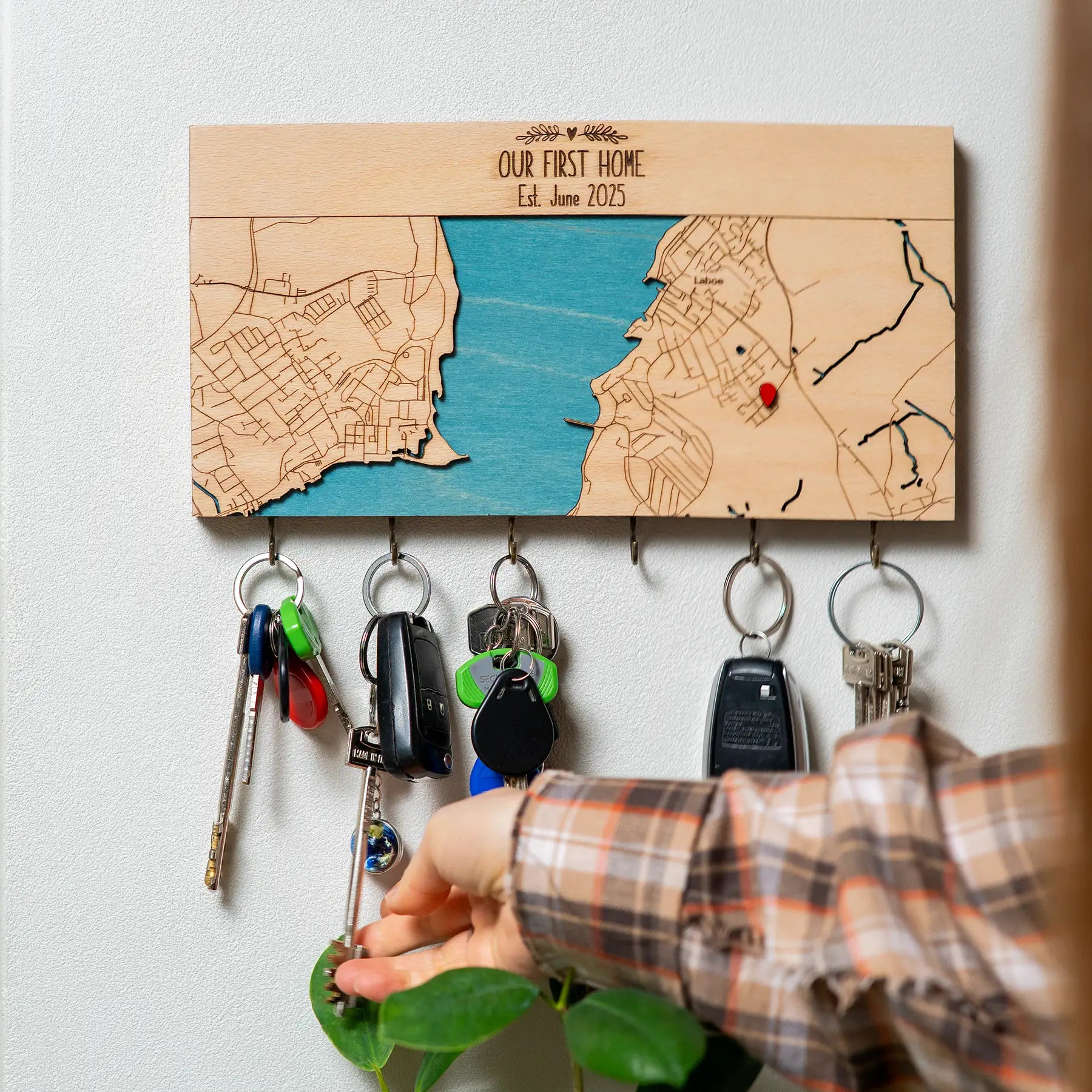 Hand placing keys on wall mounted wooden key holder with hooks and custom home map