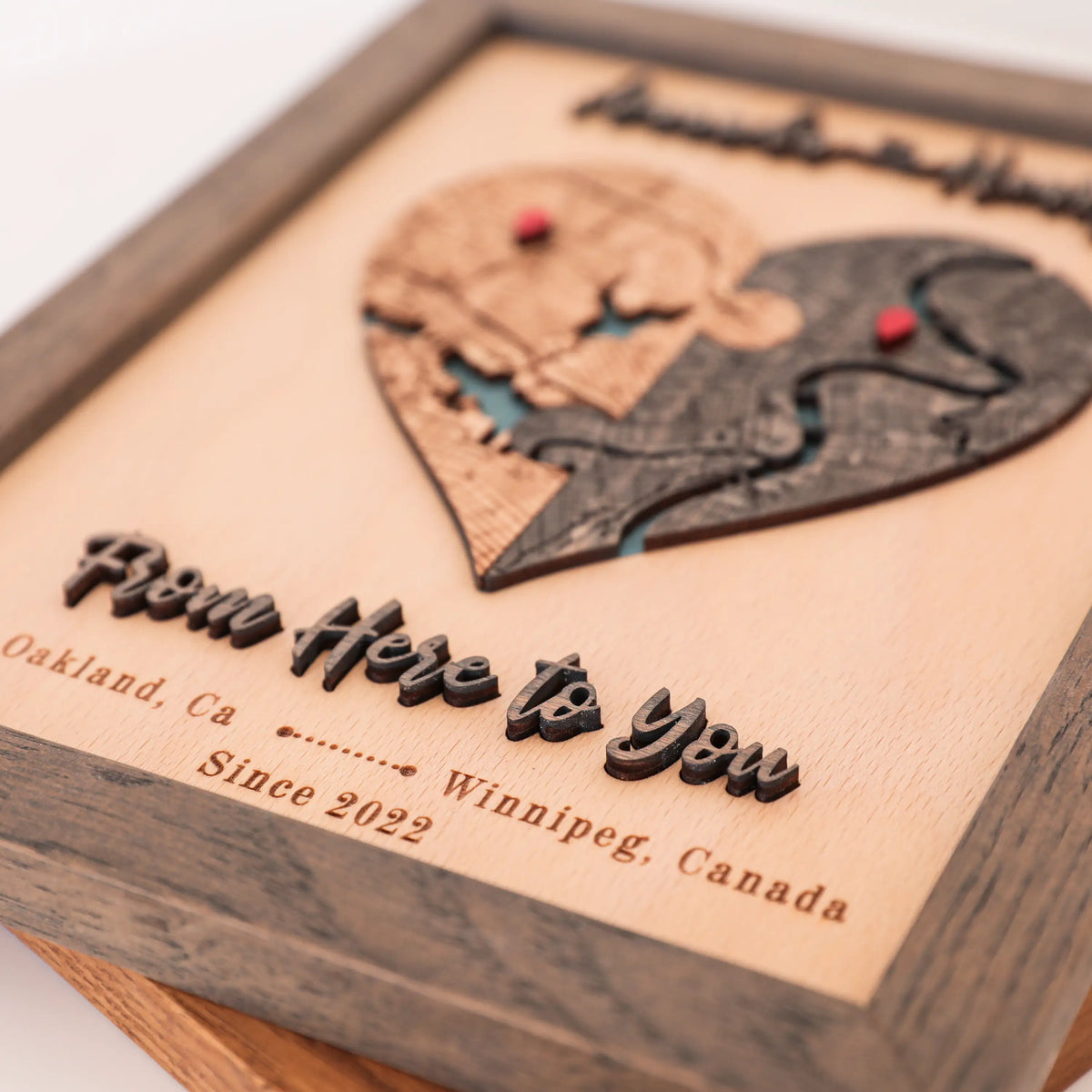 Close-up of personalized wooden love story map with raised 3D lettering, custom locations, and grey oak frame.