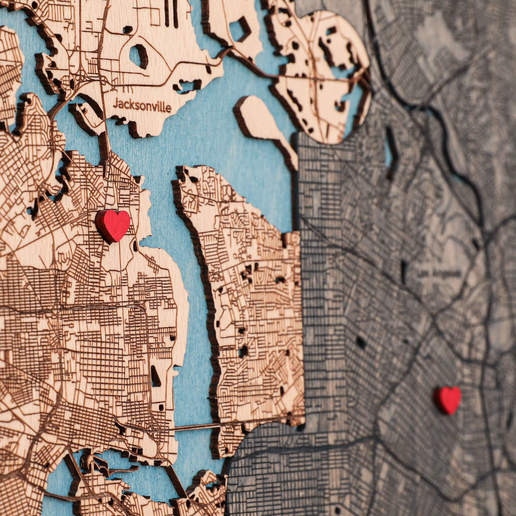 Close-up of personalized wooden map with detailed streets, blue water, red heart pins, and two custom locations.