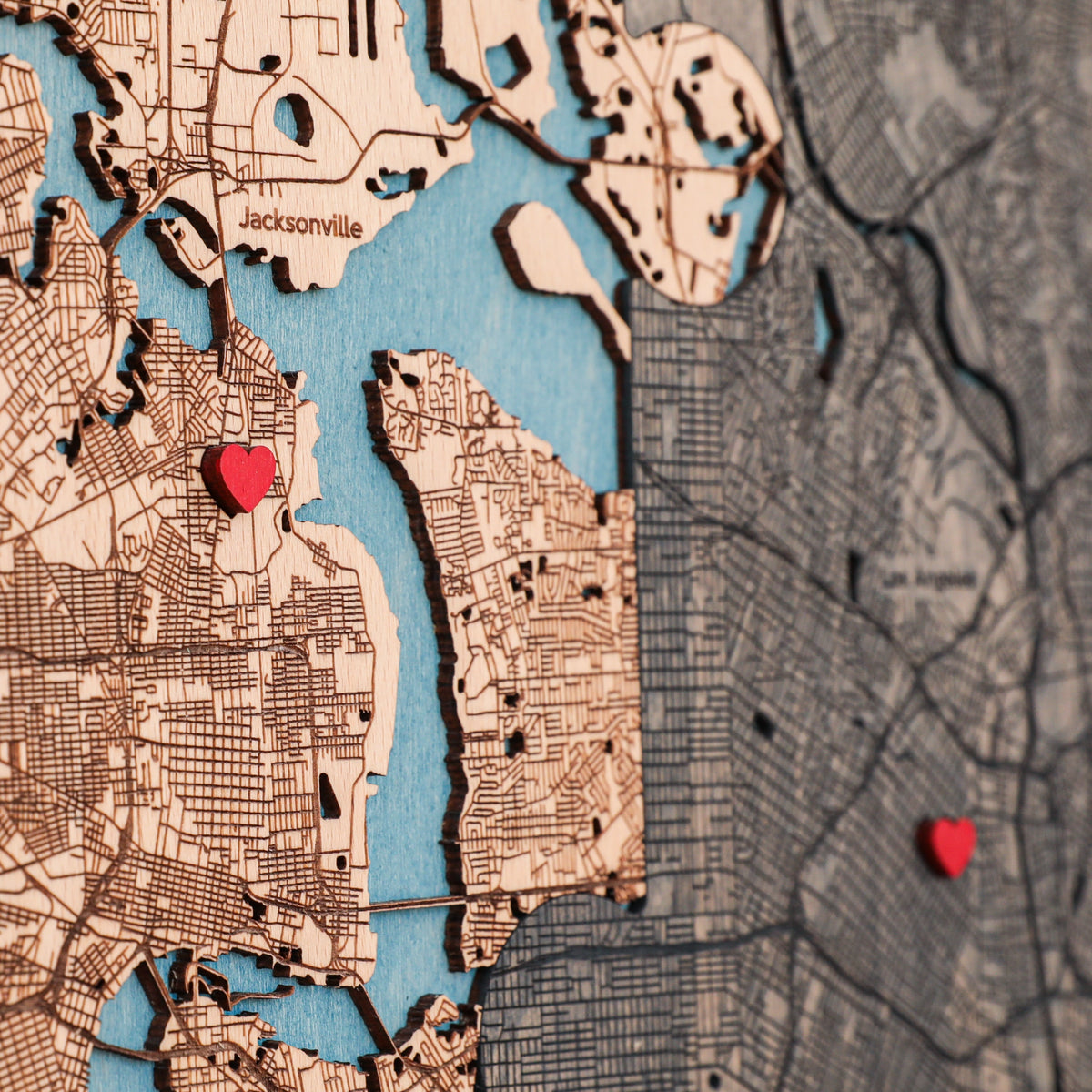 Close-up of personalized wooden map with detailed streets, blue water, red heart pins, and two custom locations.