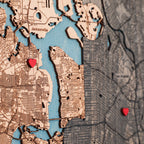 Close-up of personalized wooden map with detailed streets, blue water, red heart pins, and two custom locations.