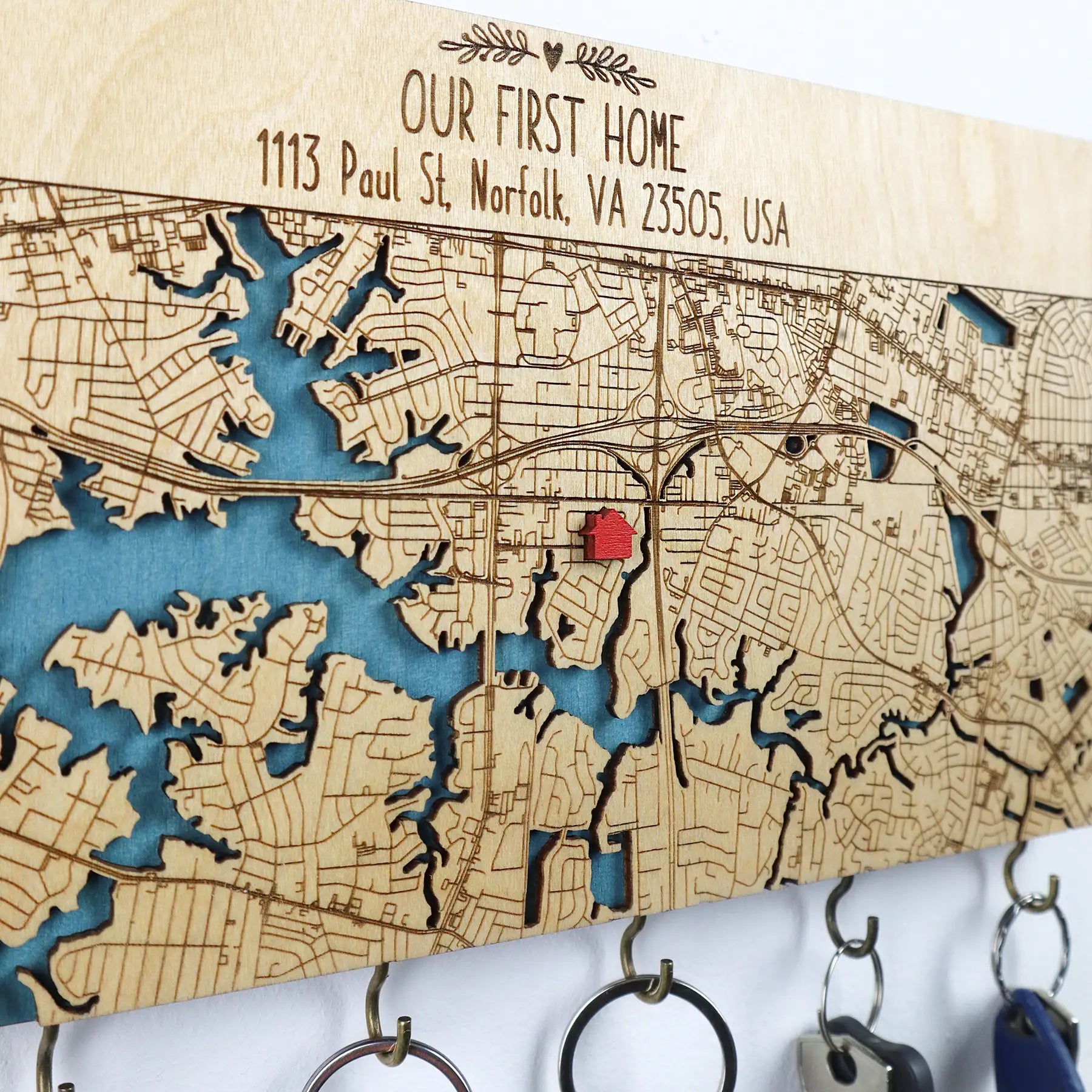 Close-up of a personalized wooden wall key holder with hooks showing engraved map detail and home location marker