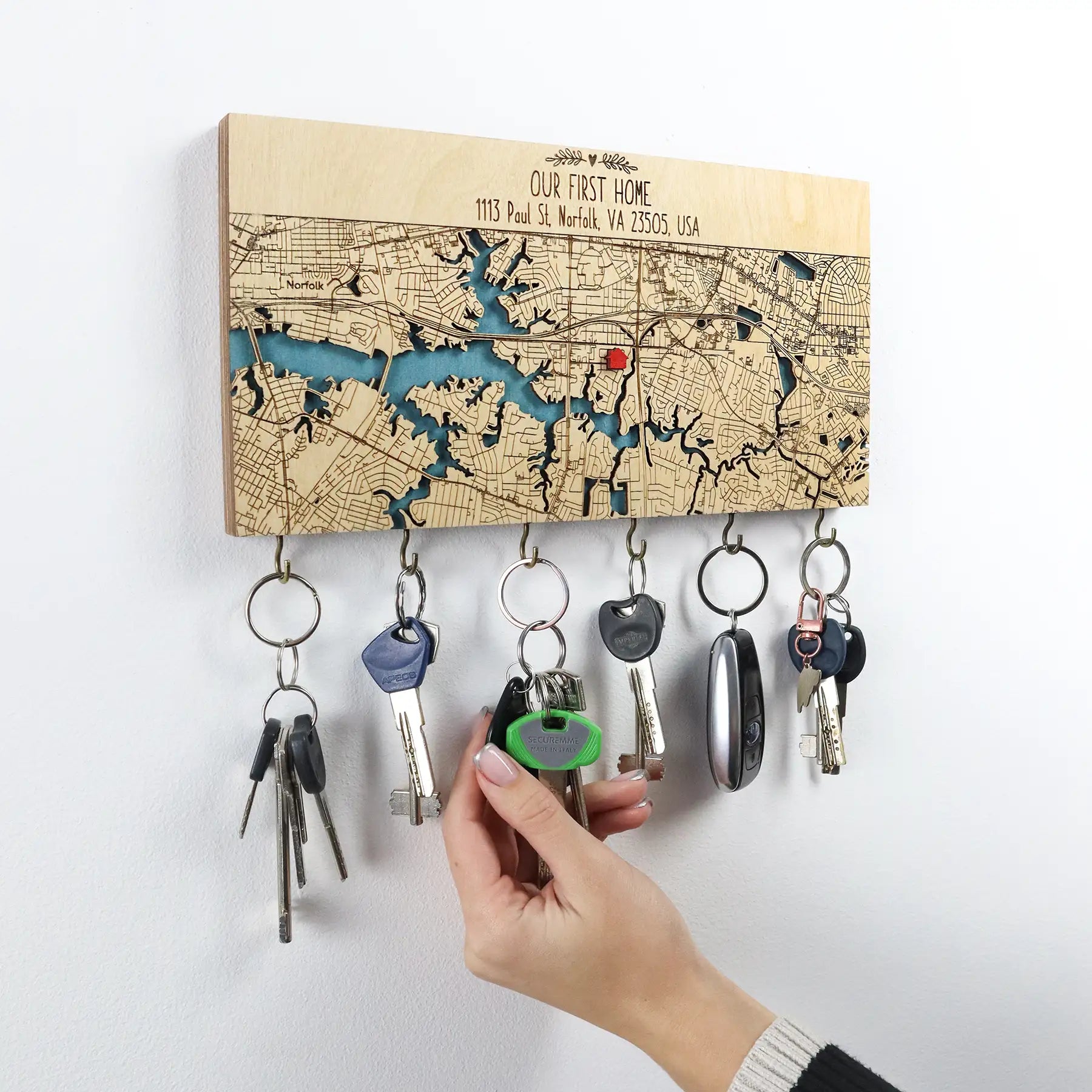 Hand placing keys on a personalized wooden wall key holder with hooks made from a custom home map