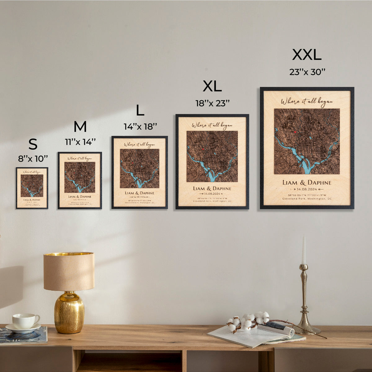 Framed maps on a wall with size labels and a lamp on a table below.