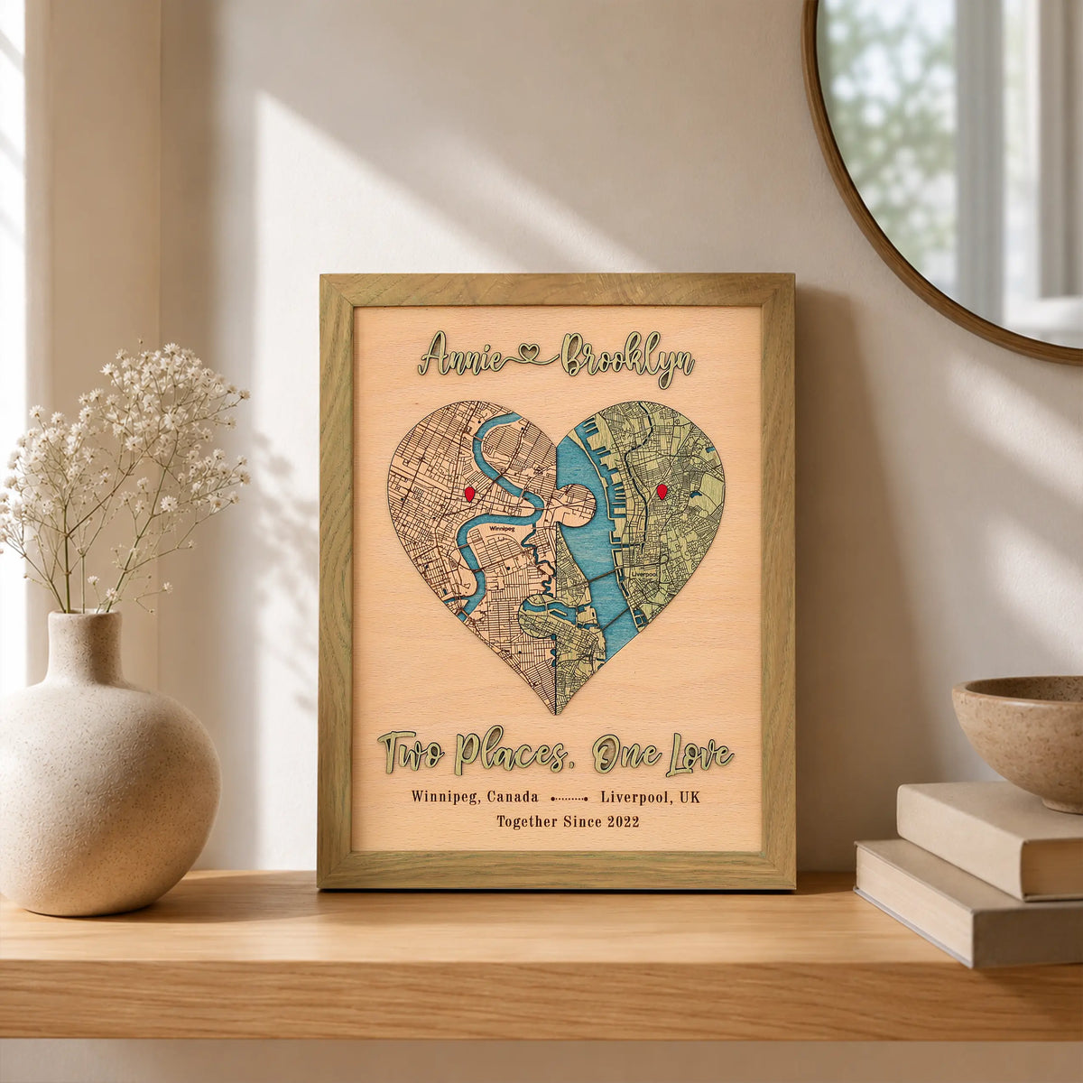 Two-location love map in sage frame displayed on a wooden shelf with raised names, red pins, and custom places.