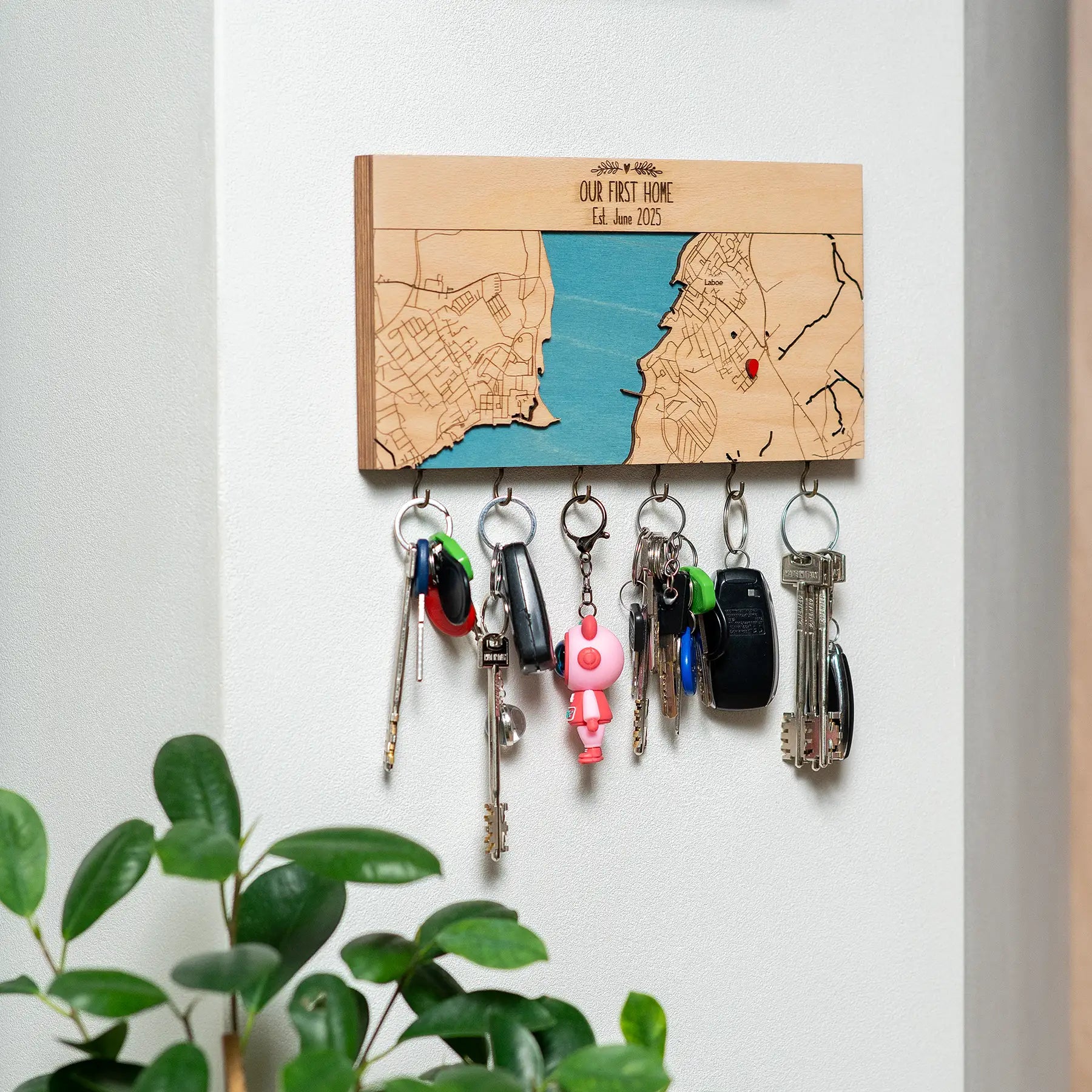Wall mounted wooden key holder with hooks displayed in entryway with hanging keys and plant decor