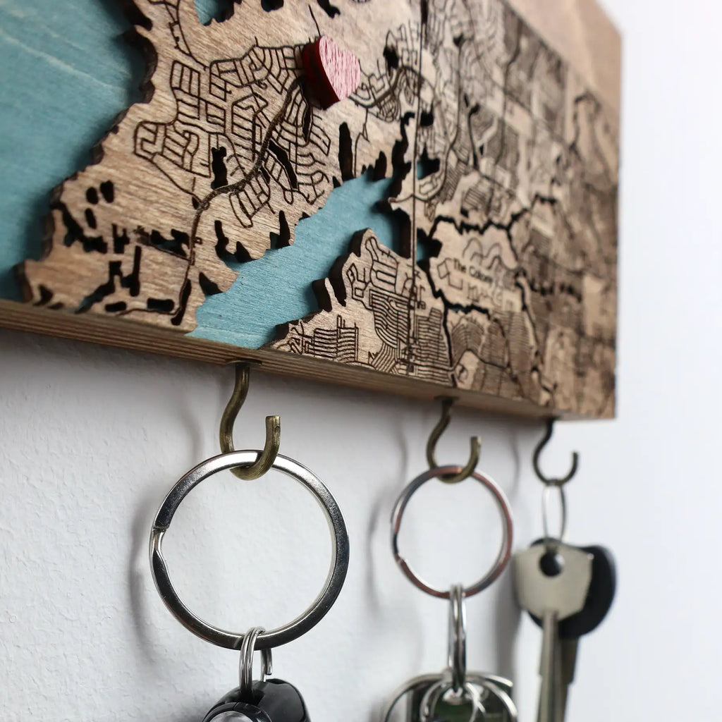 Close-up of wall mounted wooden key holder with hooks showing layered map detail and metal hooks