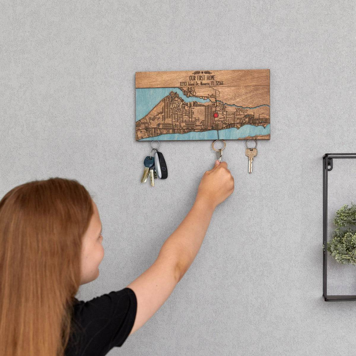 Child hanging keys on wooden key rack for wall with personalized first home map design